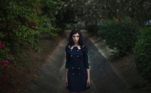 Portrait of a woman in a navy dress amidst vibrant foliage, evoking elegance and mystery in an outdoor setting.