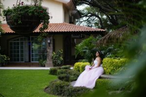 Beautiful woman in pink ball gown sitting in a garden, surrounded by lush greenery.