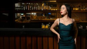 Portrait of a woman in a teal dress standing confidently at the bar, showcasing elegance and fashion.