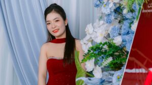 Woman in a red dress posing beside blue and white flowers indoors.