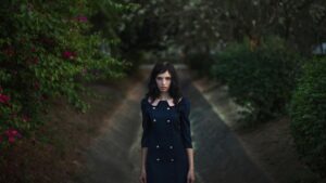 Portrait of a woman in a navy dress amidst vibrant foliage, evoking elegance and mystery in an outdoor setting.