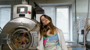 Young woman posing stylishly beside a large industrial washing machine indoors.